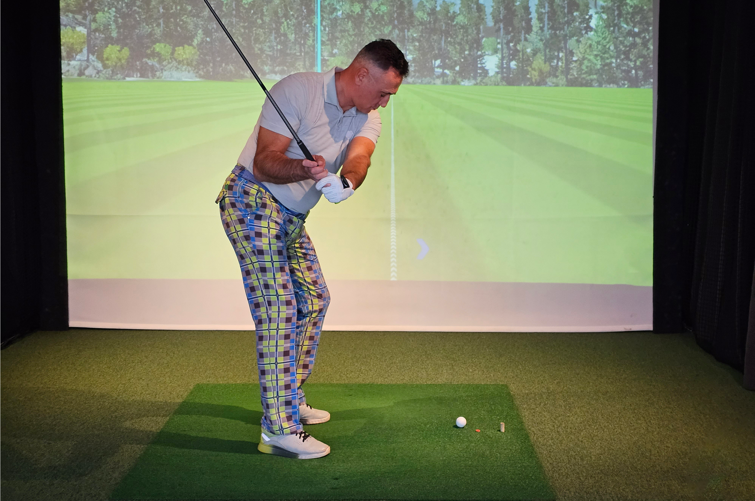 Golfer practicing swing in indoor simulator.