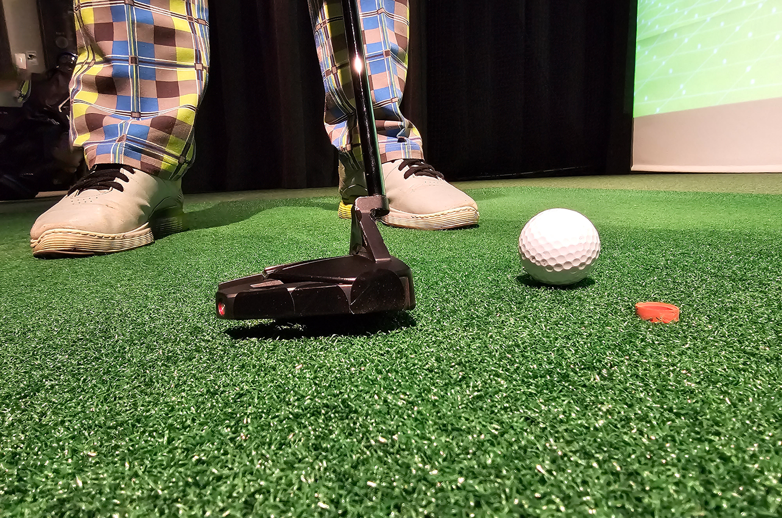 Person playing indoor mini-golf with putter.