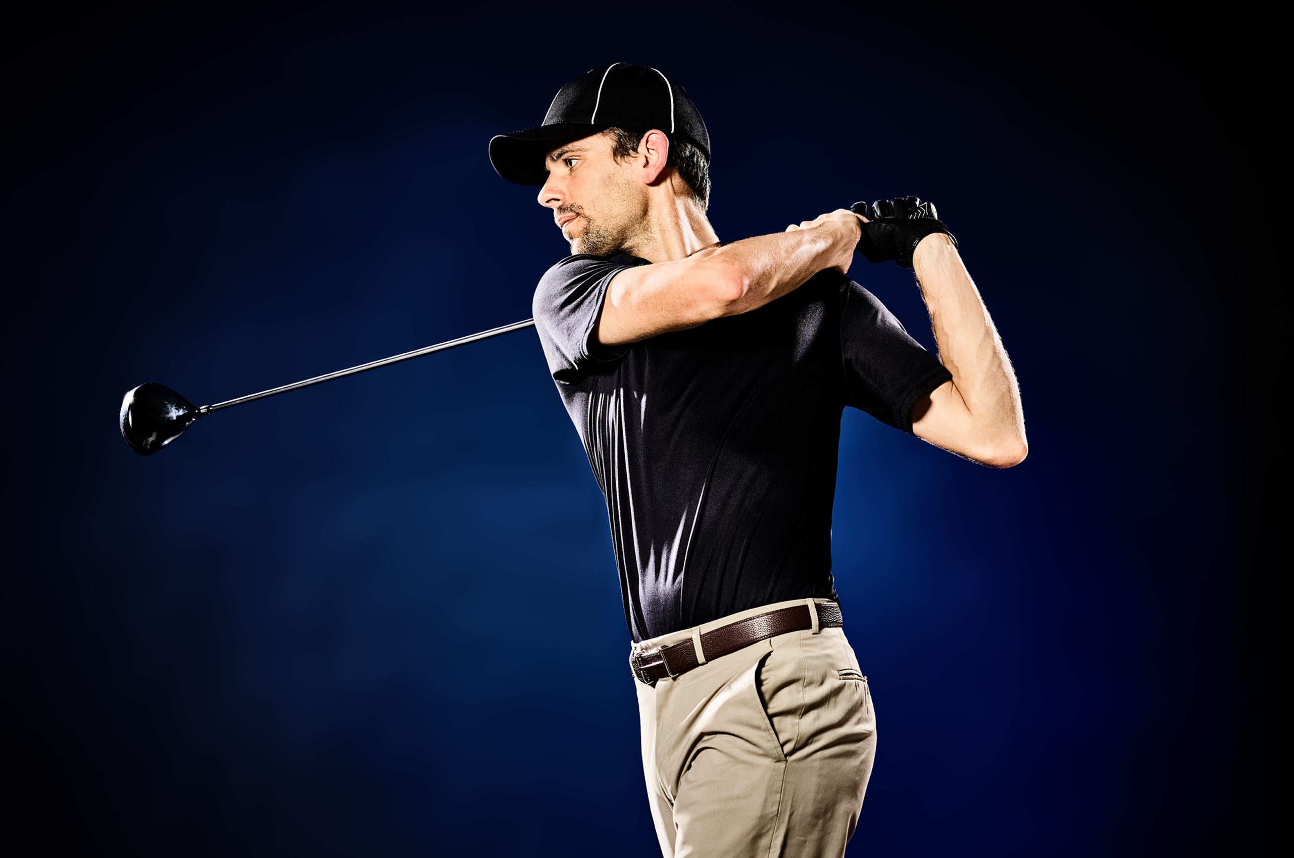 Golfer swinging club on dark background.